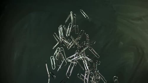 Falling Silver Paper Clips Against a Dark Green Background