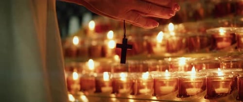 Female hands holding a wooden religious cross near burning glowing candles in the Temple of the Lord
