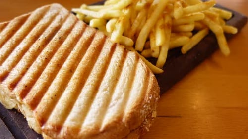 Gegrilltes Panini-Sandwich und knusprige Pommes frites, wunderschön serviert auf einem Holzbrett