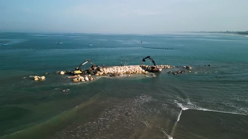 Luftaufnahme einer Küstenbaustelle mit Baggern beim Bau einer Felsbarriere