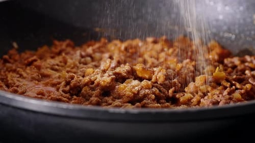 Ground meat cooking in pan with seasoning being added