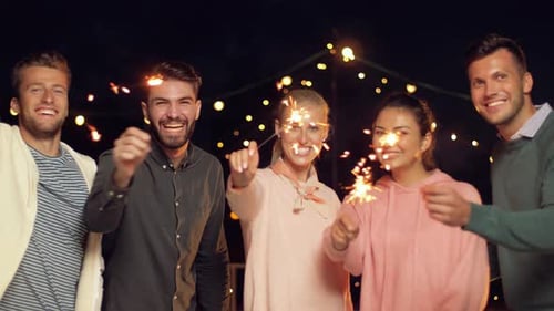 Leisure, Celebration and People Concept - Happy Friends with Sparklers at Rooftop