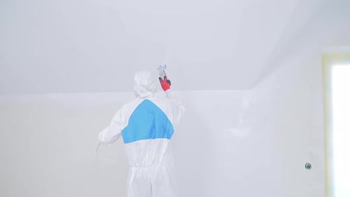 Painter spraying white paint in an indoor room