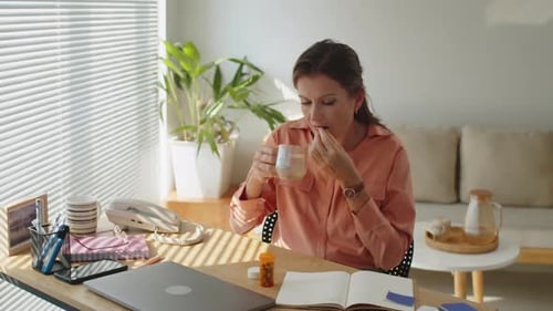 Woman Takes Pills at Desk by Sunny Window