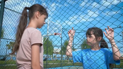 Children Staring Through Wire Fence on Sunny Day