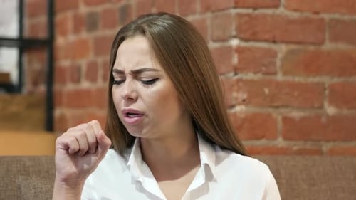 Young Woman Coughing Indoors with Brick Wall Background