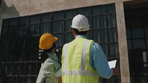 L'architecte et l'ingénieur travaillent ensemble sur des plans d'étage à l'extérieur du bâtiment du chantier