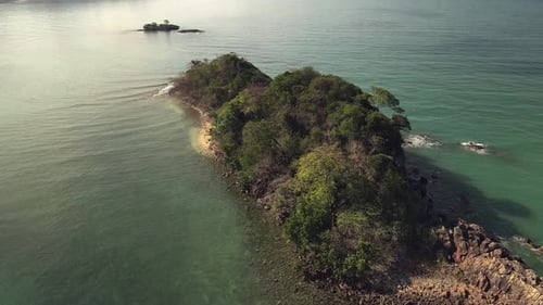 aerial right orbit, birds eye view of small tropical island with small beach and rocky coastline