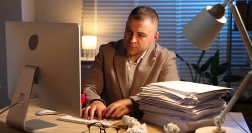 Bourreau de travail. Un homme submergé allongé sur une pile de documents près d'un ordinateur devant un bureau en bois à l'intérieur