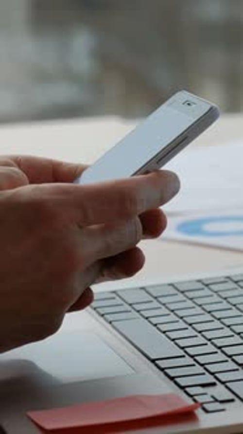 Hands Holding Phone Near Laptop In Office