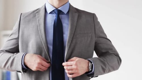 Businessman in suit fastening jacket button and adjusting necktie at the office