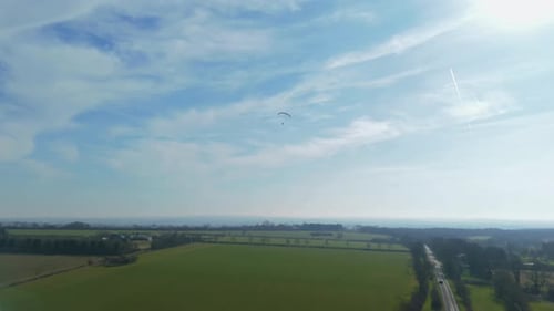 Aerial video high above the village as a paraglider soars peacefully across a wide open sky.