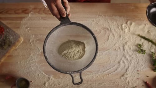 Unrecognizable baker sifting flour on cutting board in pizza restaurant kitchen