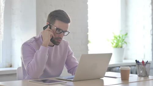 Young Adult Working on Laptop and Talking on Phone