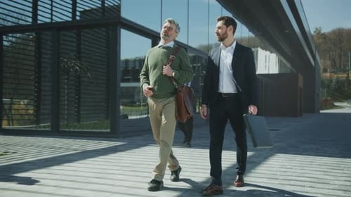 Partners Review Plans with Gestures Two Professionals Collaborate on Project Outside in Bright