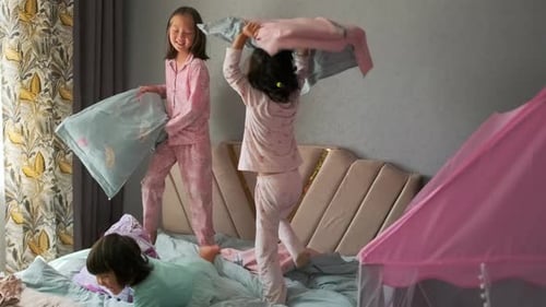 Des adolescentes ont un oreiller, se battent contre trois petites sœurs, filles asiatiques sautant sur le lit ensemble