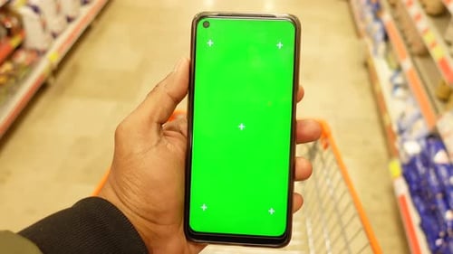 Hand Holding Mobile Phone with Green Screen While Shopping at Supermarket