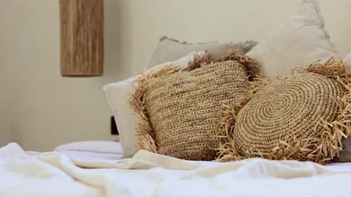 Close-up of beautiful straw handmade boho style pillows on messy bed in exotic Bali villa