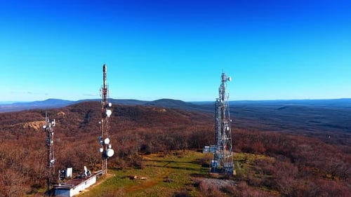 Telecommunication towers on forested hill under clear blue sky.