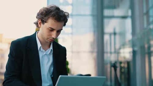 Caucasian Man Sitting on the Bench Working on the Laptop Near the Business Centre
