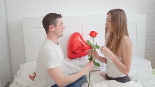 Man Presents Rose to Woman on Bed