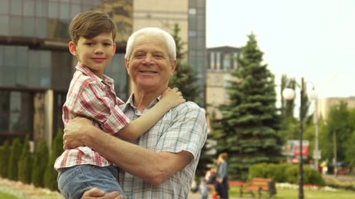 Smiling Grandfather Holding Grandson Waving in City Park