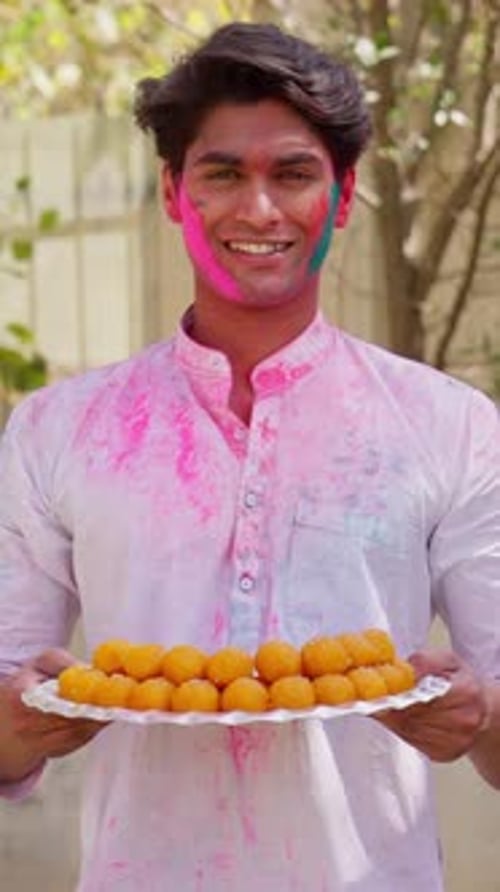 Vidéo verticale d'un Indien tenant des bonbons Thali avec de la couleur Holi sur son visage