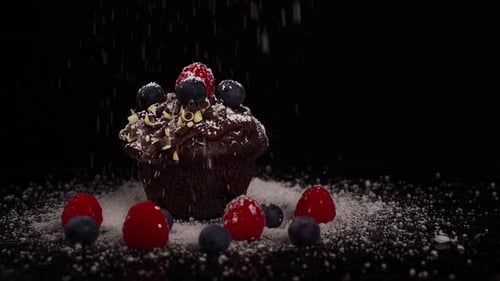 Close-up shot of a chocolate muffin with red fruits all around, powdering white sugar in slow motion