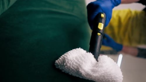 Vertical Video in an Apartment Cleaner in a Yellow Apron Does a Steam Cleaning of a Green Sofa with