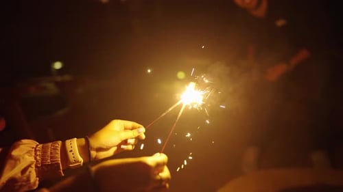 Girl's hands holding party sparklers glowing at night for celebration, slow motion