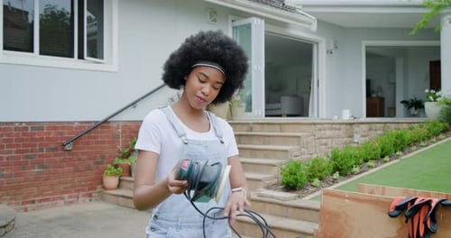 Mulher afro-americana em jeans encontrando um cabo de lixadeira enrolado, cordão desenrolado no pátio, preparando o DIY