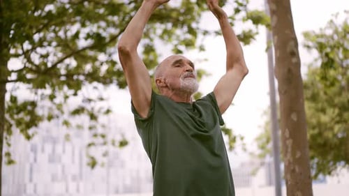 Man Stretches Arms Upward in Urban Green Park
