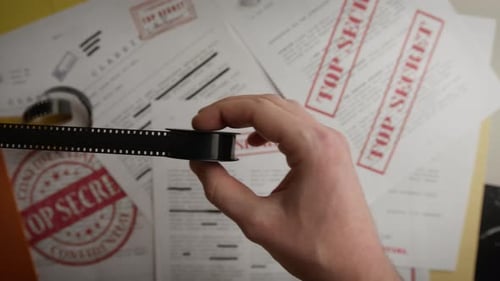 Hand Showing Film Strip Over Secret Documents