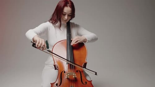 Beautiful Woman Sitting and Playing the Cello in a Studio on a White Background