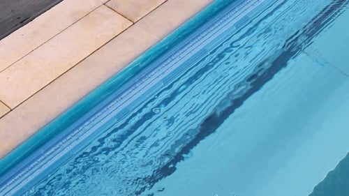 Close-up of a pool edge with an automatic cover and bubbles on the surface. The water gently ripples
