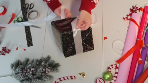 Hands Tying White Ribbon on Black Christmas Gift