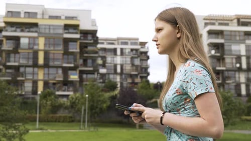 A Beautiful Young Caucasian Woman Works on a Smartphone As She Walks in a Suburban Area