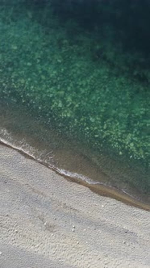 Aerial Vertical View of Beach with Wave Caressing Shore Sun Glare Small Waves on the Water Surface