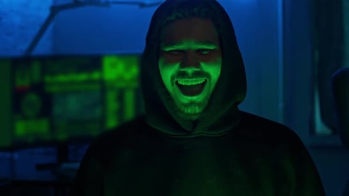 Retrato de um hacker sorridente em pé na frente de seu equipamento de computador em seu covil