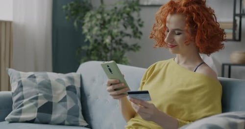Joyful Woman Shopping in Online Store Making Payment with Credit Card Using Smartphone at Home