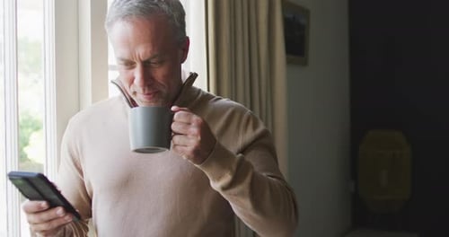 Man Drinking Coffee and Using Cell Phone Indoors