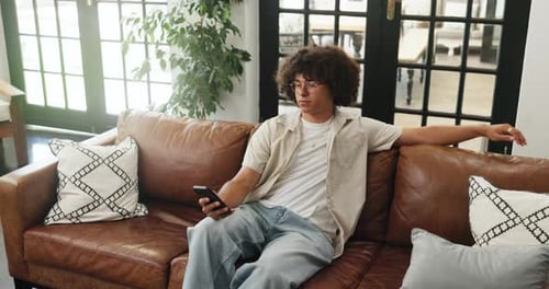 Young Man Relaxing on Couch Using Mobile Phone
