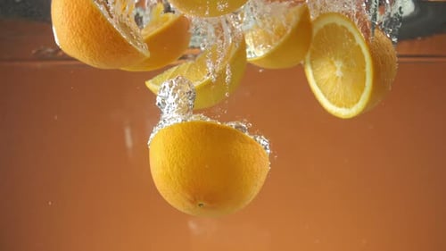 Slow motion of fresh sliced Oranges falling into water on orange background