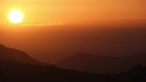 Grand soleil se couchant derrière un nuage au crépuscule dans un paysage vallonné