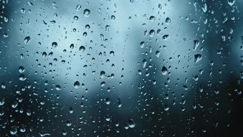 Regentropfen auf Glasfenster mit verschwommenem Stadthintergrund bei Regenwetter