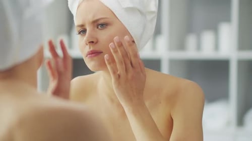 Junges Mädchen sitzt vor einem Schminkspiegel im Badezimmer und trägt eine Hautcreme auf