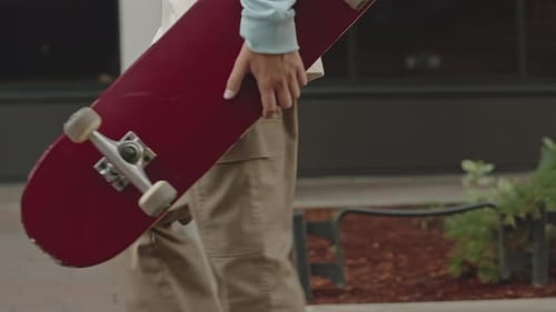 Teenage Boy with Skateboard Strolling along Street