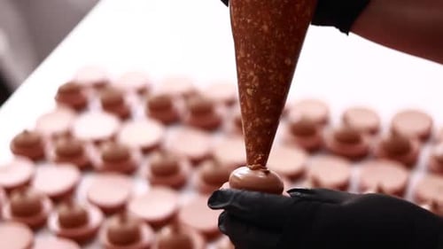 Close up of chef hands putting salt caramel with nuts in ganache cream on chocolate macarons shells.
