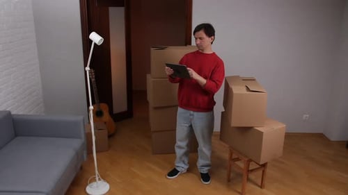 Man Using Digital Tablet While Organizing New Home with Cardboard Boxes