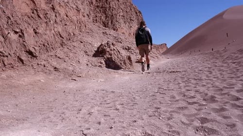 Lone man hikes along red sand desert rock cliff, Atacama region, Chile